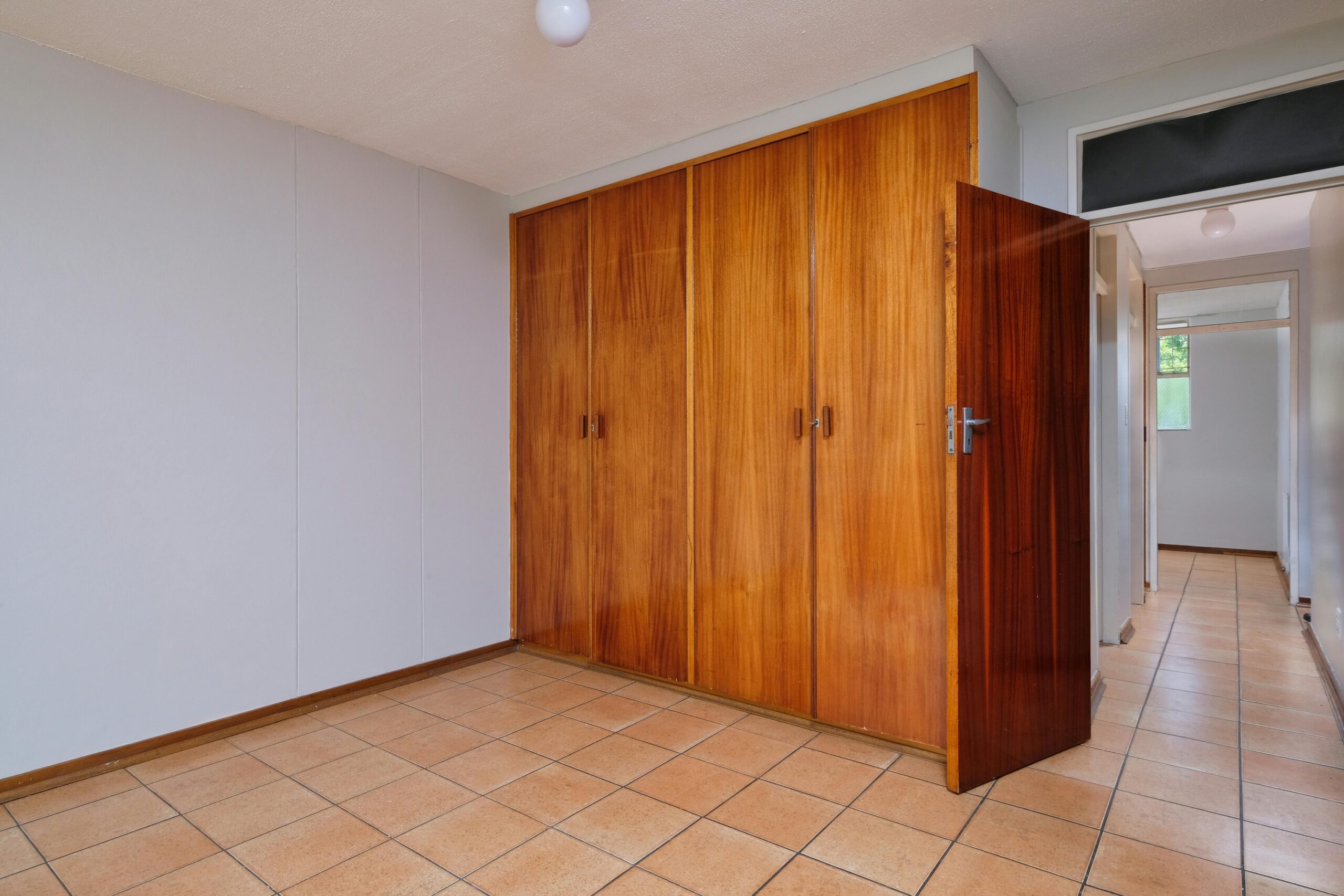 Bright interior room featuring wooden wardrobes and a tiled floor, ideal for real estate showcase.